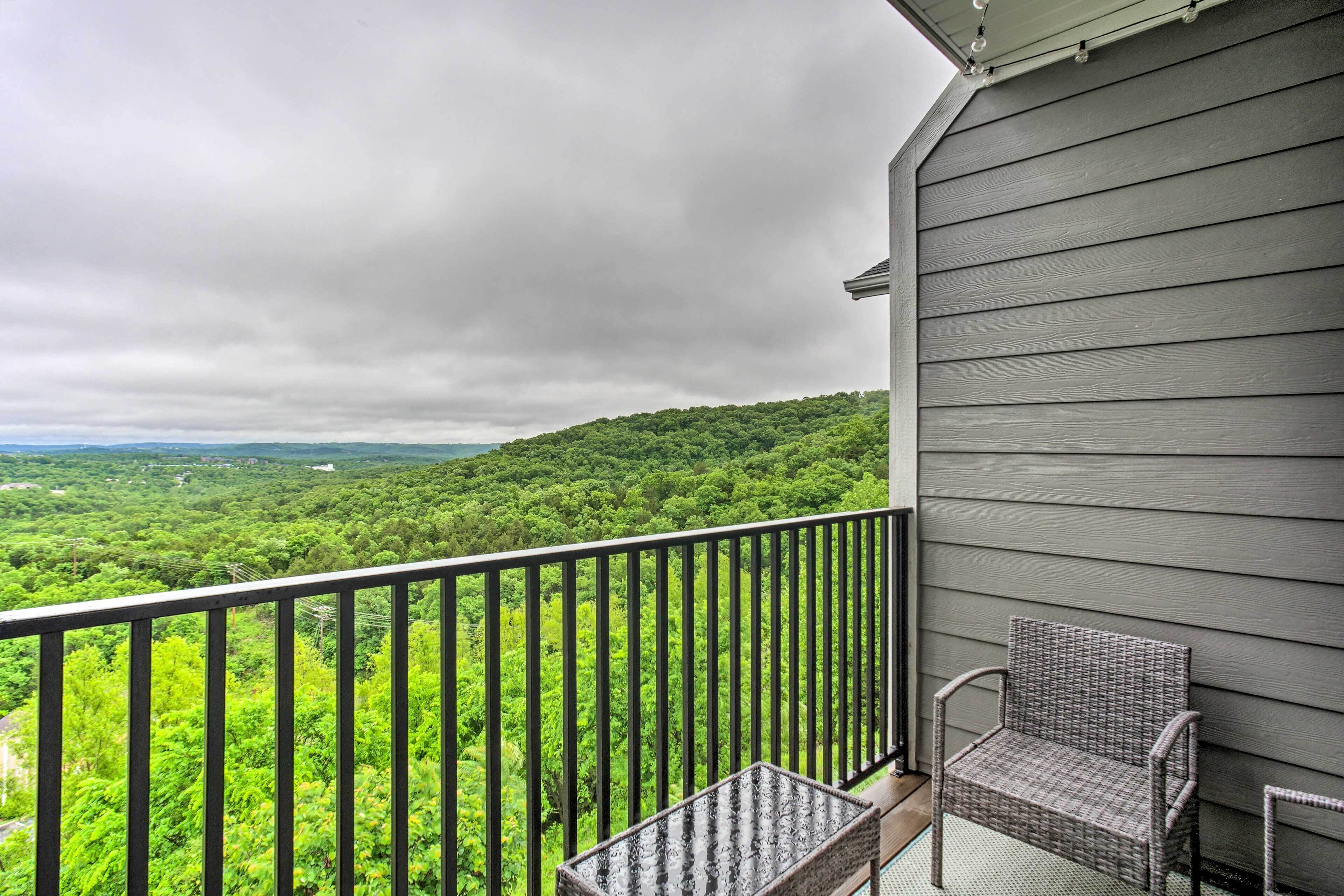 Un balcon avec un fauteuil en osier et une petite table, donnant sur un paysage verdoyant et luxuriant.