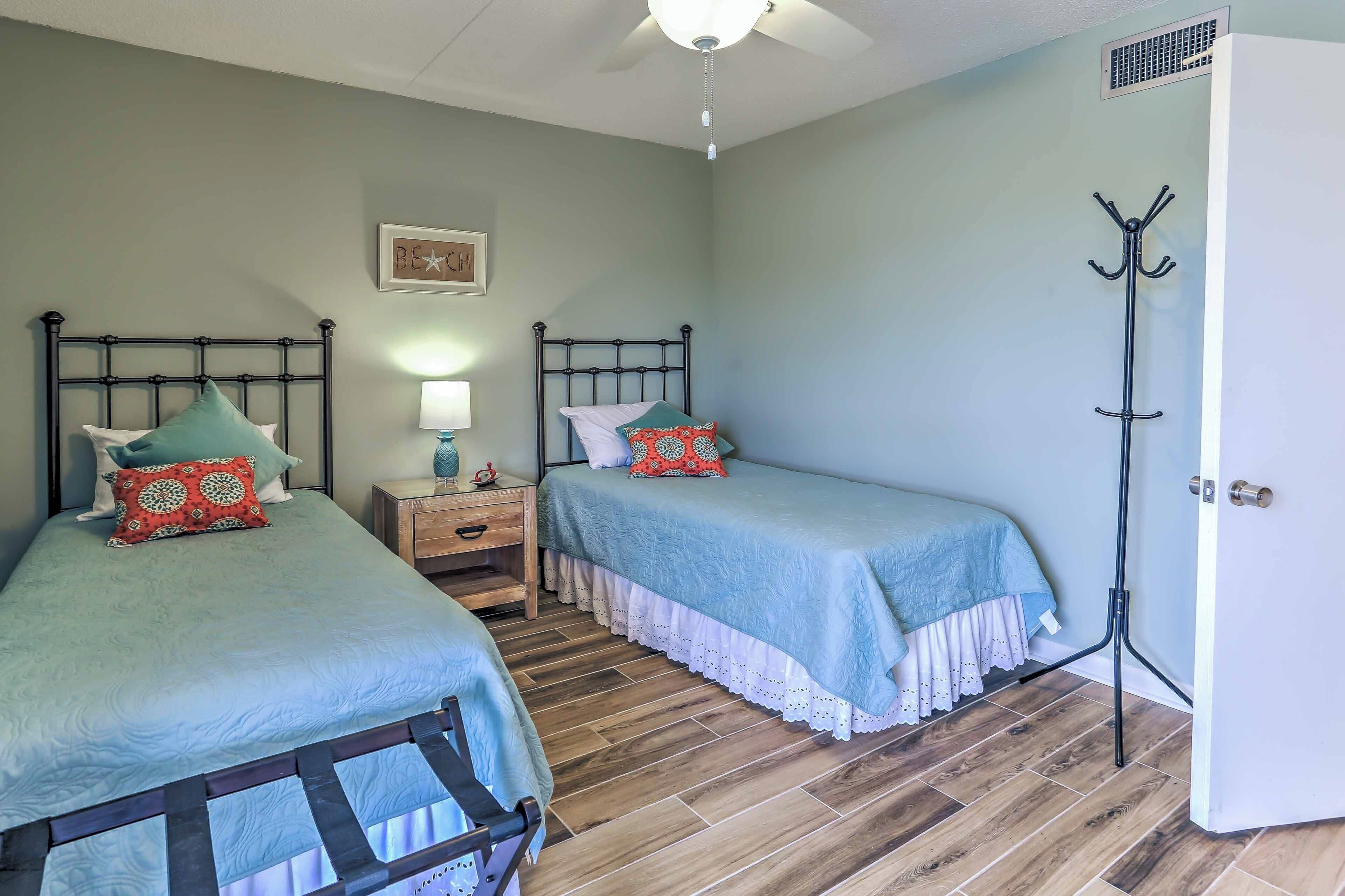 A bedroom with two beds, a nightstand, a lamp, and a coat rack.