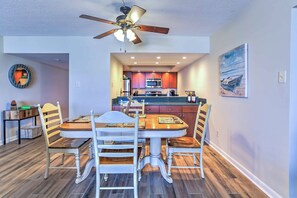 A dining area with a round table and chairs, a ceiling fan, and a kitchen in the background. - Chic Myrtle Beach Seaside Escape w/ Pool Access! (Myrtle Beach)