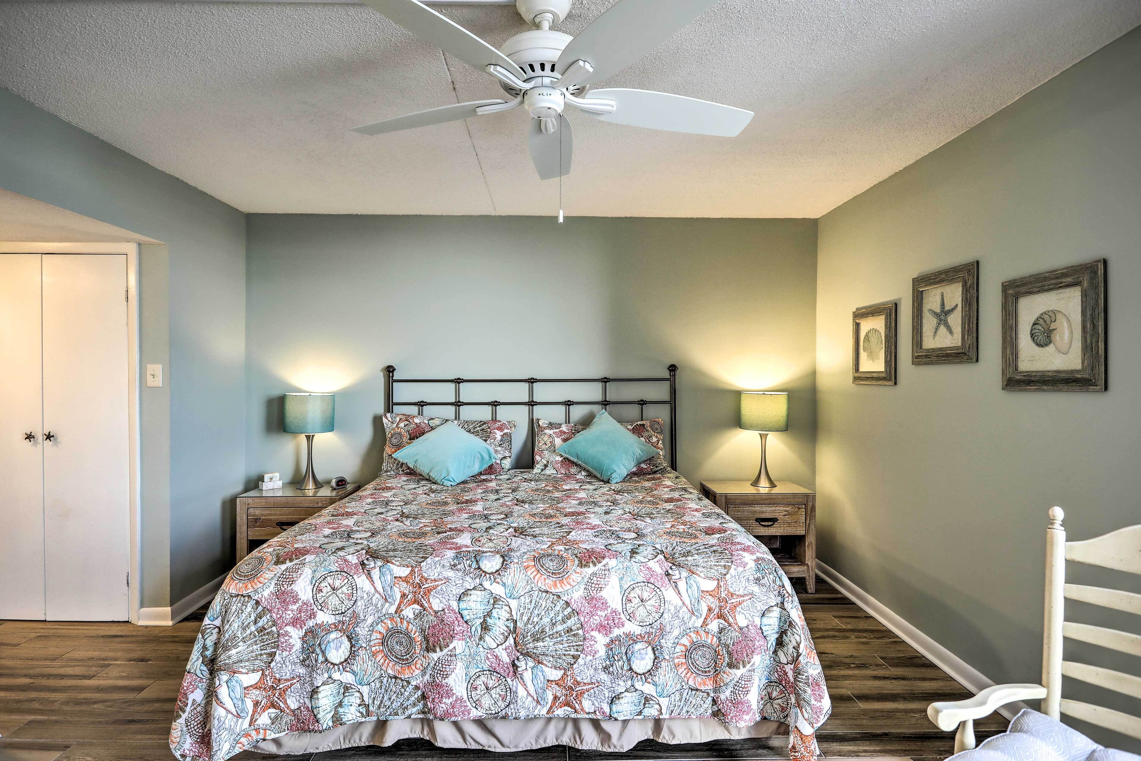 A bedroom with a bed, two bedside tables, a ceiling fan, and framed pictures on the wall.