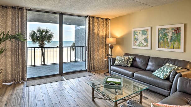 Een woonkamer met een glazen salontafel, een leren bank, uitzicht op het strand en een deur naar een balkon.