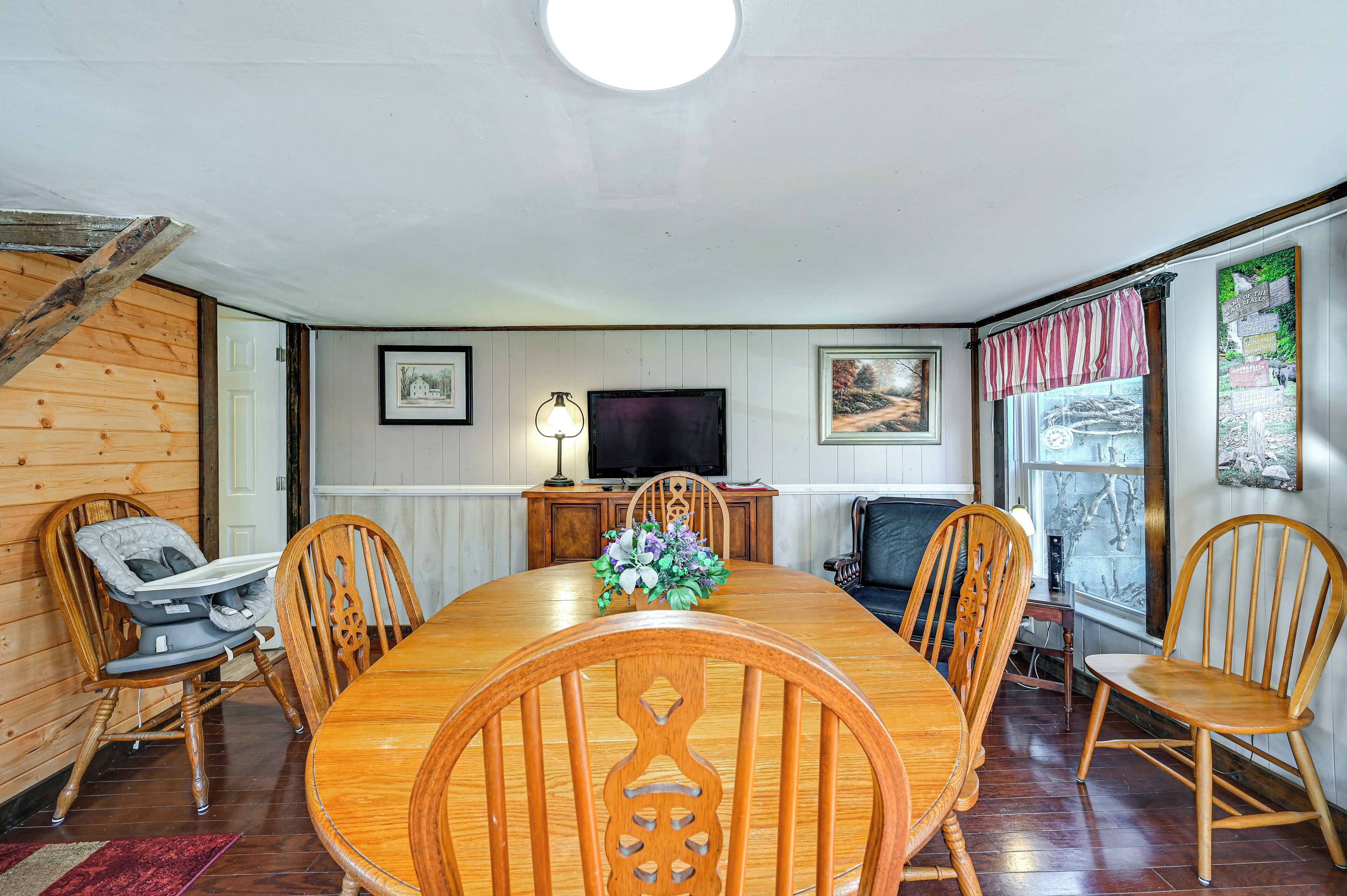A dining room with a wooden table and chairs, a television, and a window with curtains.