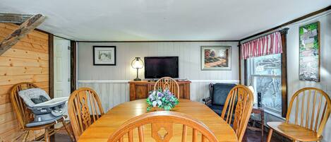 A dining room with a wooden table and chairs, a television, and a window with curtains.