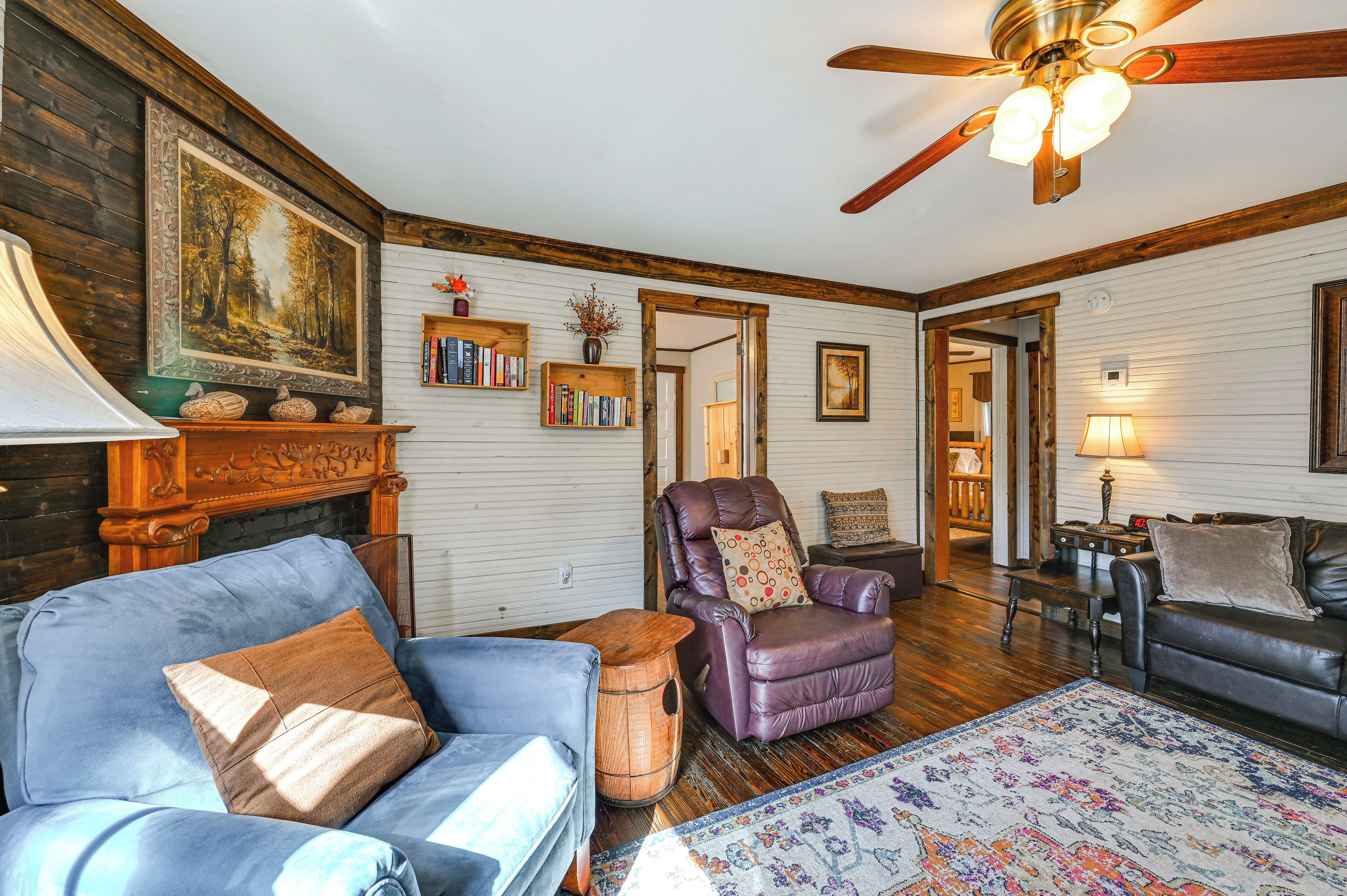 A cozy living room with a fireplace, leather furniture, a ceiling fan, and a bookshelf.