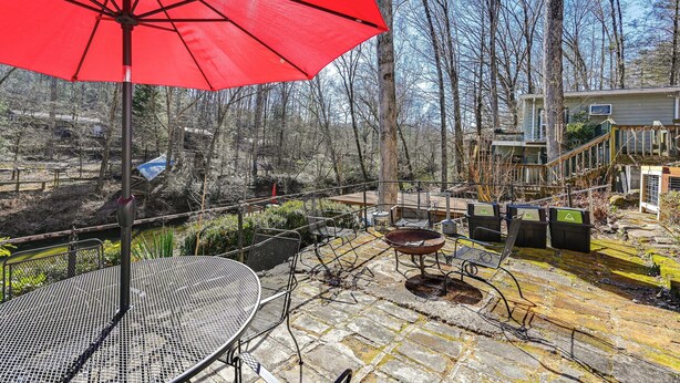 Un espace patio avec un parasol rouge, des chaises en métal, une table et un foyer.
