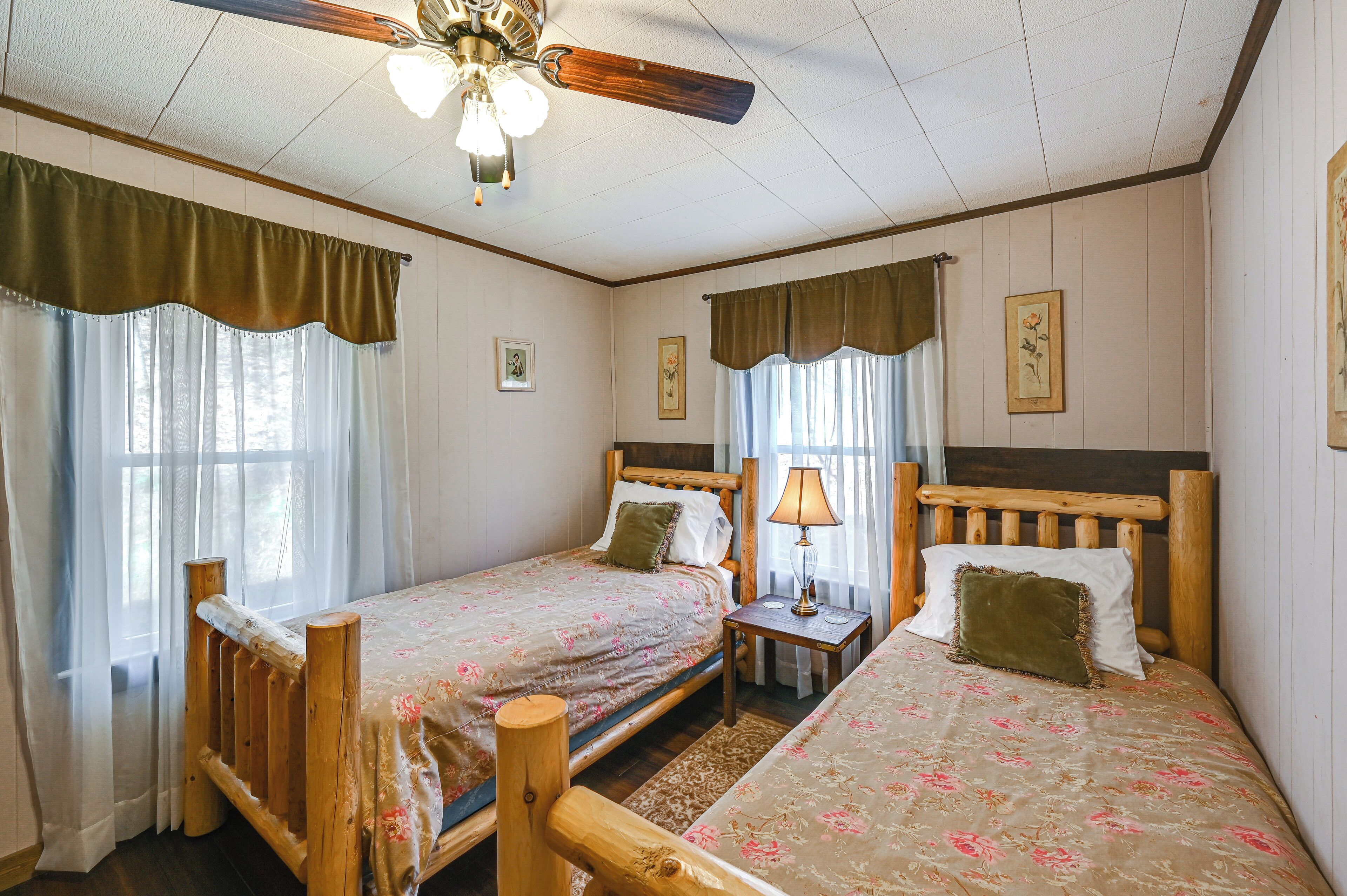 Una habitación con dos camas de madera, cada una con una mesita de noche, una lámpara y una ventana con cortinas.