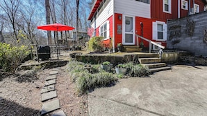 Une maison rouge et blanche avec un chemin de pierres menant à la porte d’entrée, entourée de plantes en pot et d’un parasol rouge.
