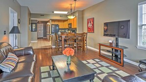 A living room with a leather sofa, a coffee table with a vase of flowers, a TV on a stand, and a kitchen in the background. - 10 Mi to Beach: Legends Resort Condo on Ninth Hole (Myrtle Beach)