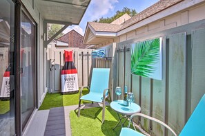A patio area with a glass door, a small table with two chairs, and a bottle of wine.