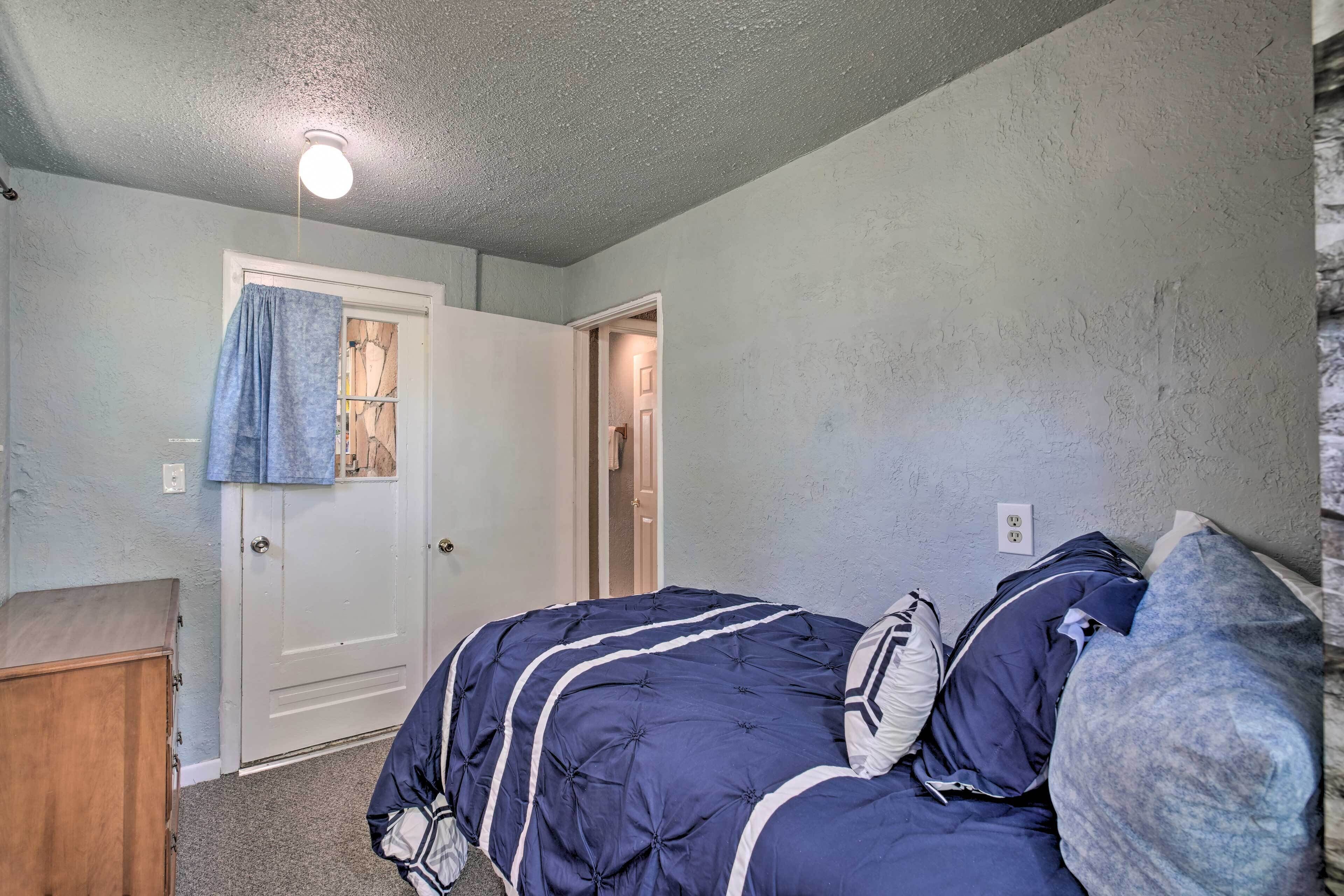 A bedroom with a bed, a wooden dresser, and a door leading to another room.