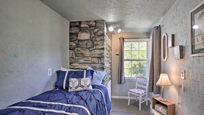 Ein Schlafzimmer mit Steinwand, einem Bett mit blauer Bettdecke, einem Sessel und einem Nachttisch mit Lampe.