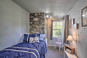 Un dormitorio con una pared de acento de piedra, una cama con colcha azul, una silla y una mesita de noche con lámpara.