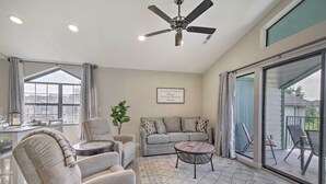 Un salon spacieux doté d’un ventilateur de plafond, d’un canapé gris, d’une table basse et d’un coin repas avec une table et des chaises.