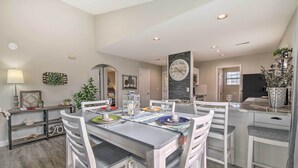 Un coin repas avec une table dressée pour quatre personnes, entourée de chaises blanches. Une horloge est fixée au mur au-dessus de la table.
