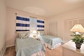 A bedroom with two beds, a nightstand with a lamp, a potted plant, and a window with striped curtains. - Condo on Lake Keowee w/ Resort Amenities & Pool! (Salem)