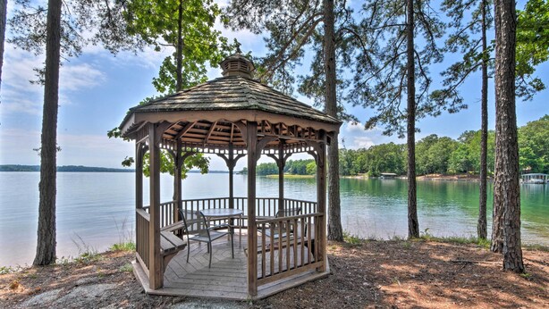 A wooden gazebo with a roof and a table and chairs, surrounded by trees and a lake. - Condo on Lake Keowee w/ Resort Amenities & Pool! (Salem)