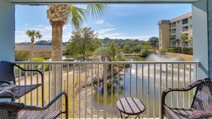 A balcony with wicker chairs and a view of a lake, surrounded by palm trees and a building. - Pool, Sauna & Beach Access: Hilton Head Condo (Hilton Head Island)