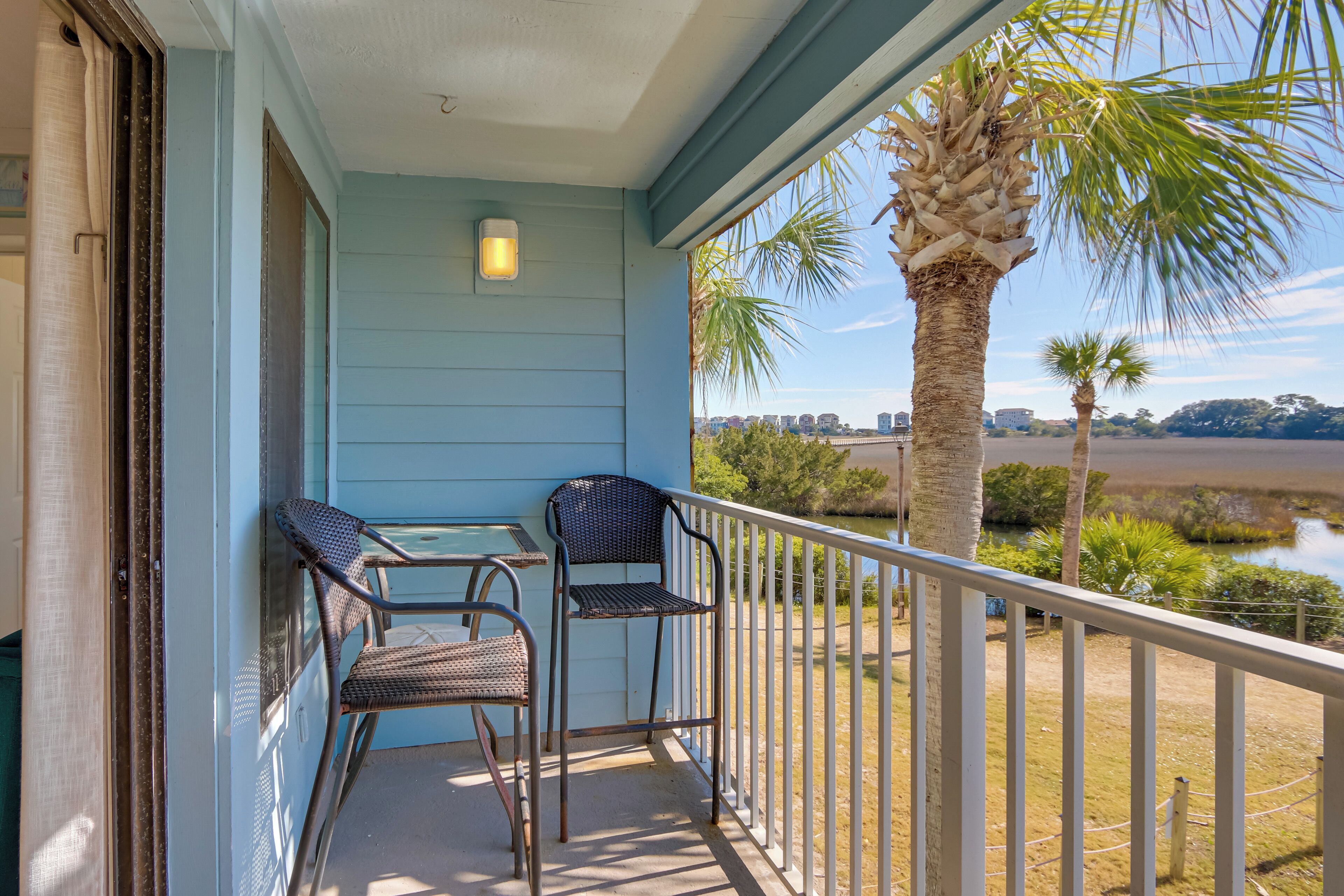 A balcony with two wicker chairs, a small table, and a railing.