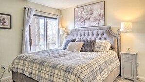 Um quarto com uma cama grande, uma mesa de cabeceira, uma luminária, um quadro emoldurado e uma janela com cortinas.