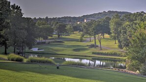 Campo de golfe com lago, árvores e um edifício ao longe.