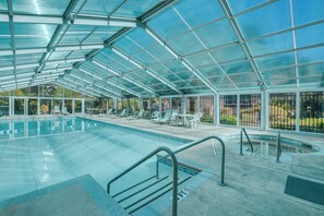 Un espace piscine couvert, doté d’une toiture en verre transparent, de chaises longues et d’un petit jacuzzi.