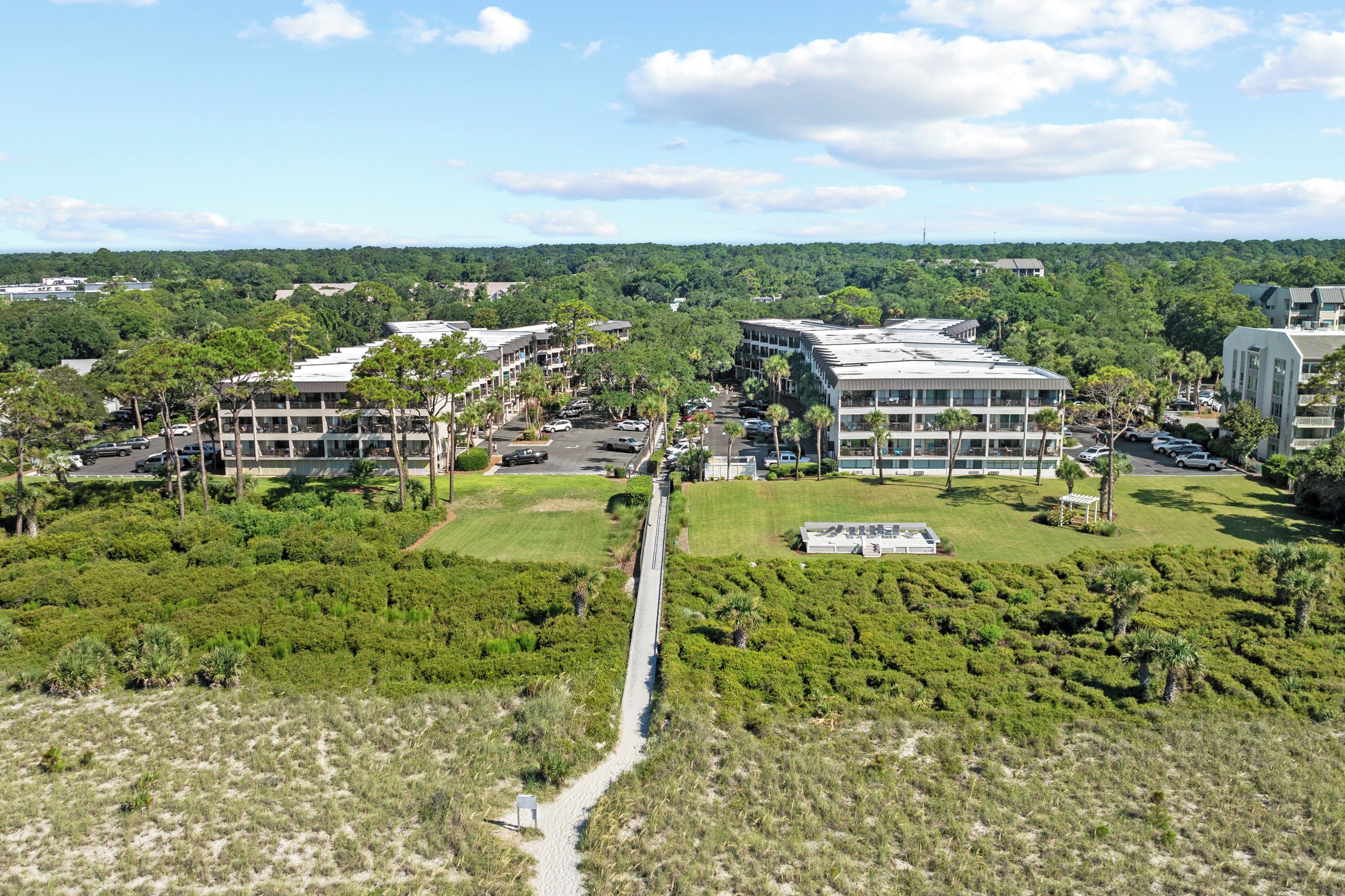 A modern building complex with multiple floors, surrounded by lush greenery and a clear sky.