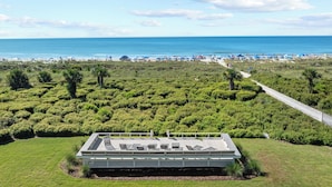 Une vue sur la plage avec un bâtiment moderne doté d’une terrasse sur le toit, aménagée avec des chaises longues.