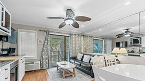 Une cuisine moderne avec des meubles blancs, un coin repas avec une table et des chaises blanches, un canapé en cuir noir et un ventilateur de plafond.