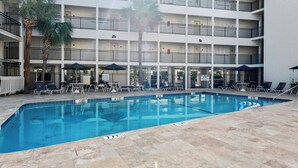 Un espace piscine d’hôtel doté de plusieurs niveaux de balcons, de chaises longues et de parasols.