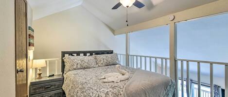 A bedroom with a bed, a nightstand, a ceiling fan, and a balcony with a railing.