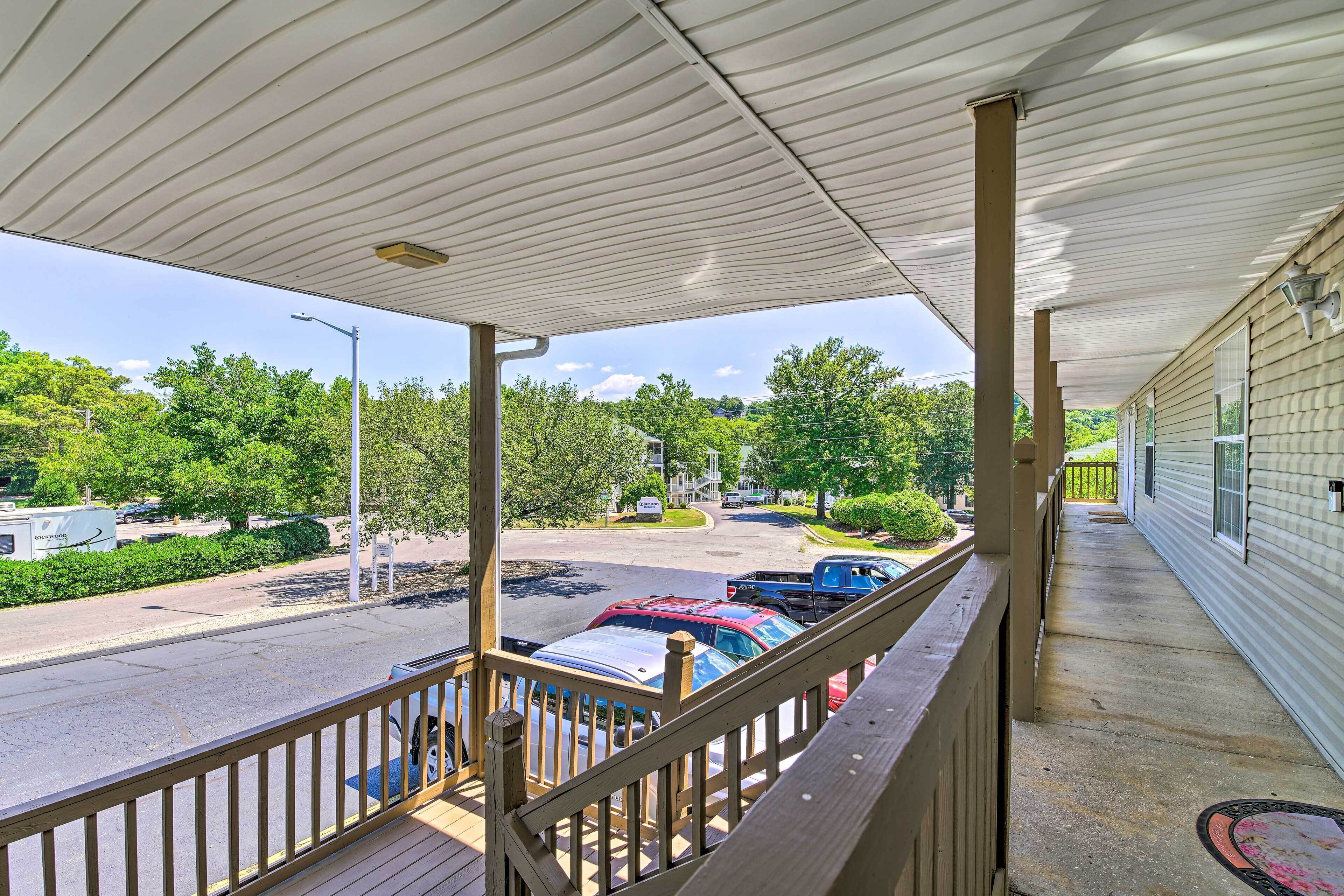 A covered porch with a view of a street and parked cars.