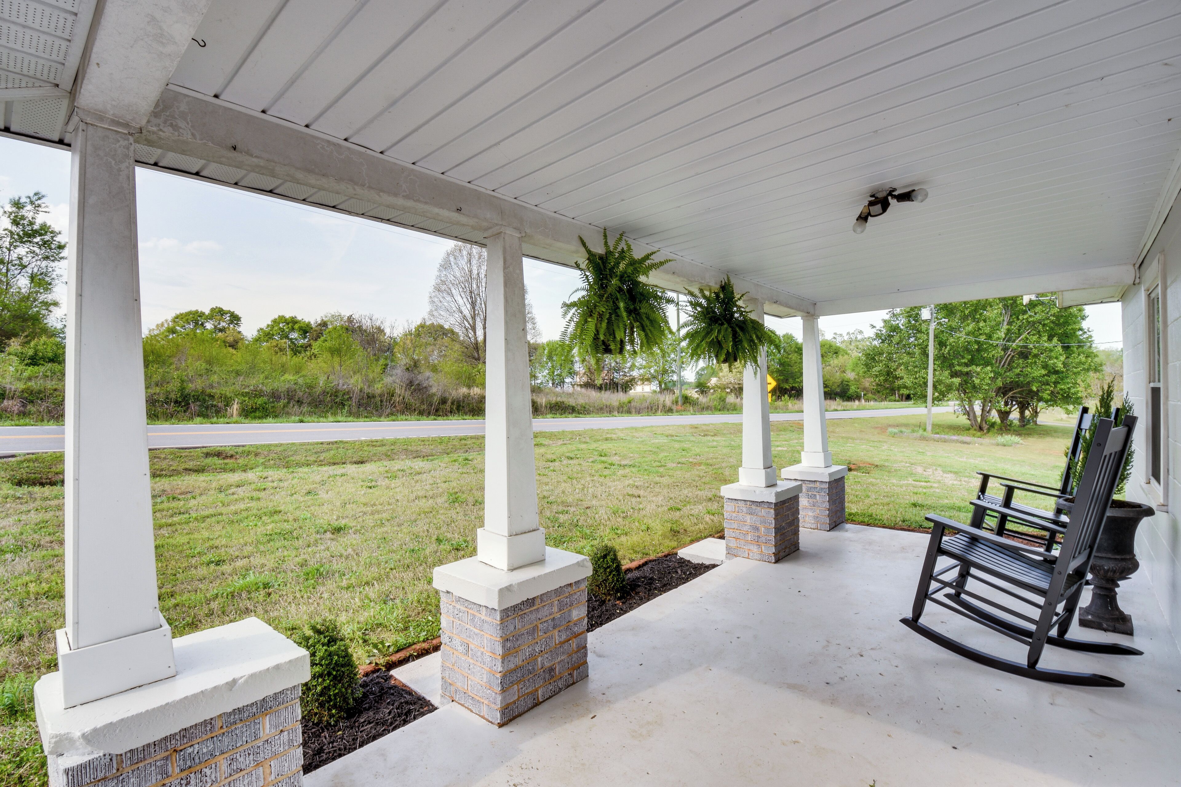 A covered porch with brick columns, a rocking chair, and hanging plants.