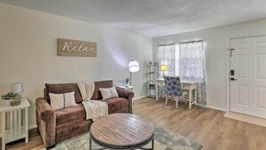 Ein Wohnzimmer mit braunem Sofa, einem runden Couchtisch, einer Lampe, einem Beistelltisch mit Pflanze und einem Schild mit der Aufschrift 'Relax'.