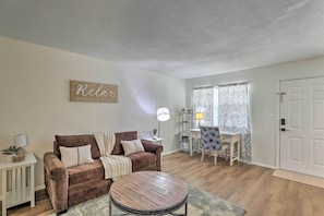 A living room with a brown sofa, a round coffee table, a lamp, a small table with a plant, and a sign that says "Relax." - Cozy Hanahan Condo w/ Cooper River Access! (Hanahan)