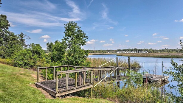 Eine hölzerne Mole führt in einen stillen See, umgeben von üppiger Vegetation und einem klaren Himmel.