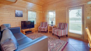 Een gezellig interieur van een chalet met een bank, twee gestreepte fauteuils, een televisie en een kleine tafel.