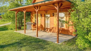 Een blokhut met een veranda, een barbecue en een schommelstoel.
