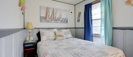 A bedroom with a bed, a nightstand, a lamp, a painting of sailboats, and a window with curtains.