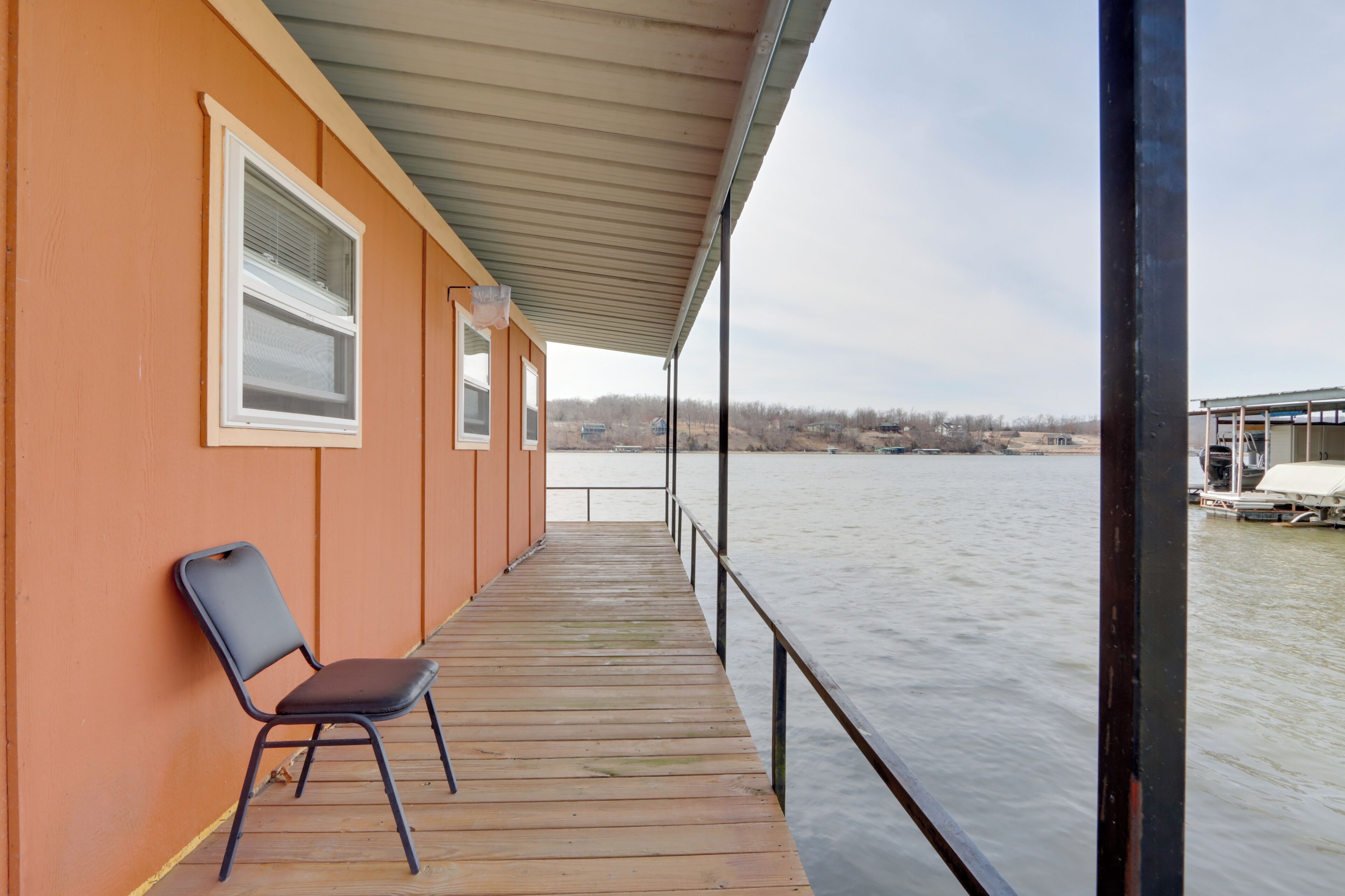 Una terraza de madera con una silla, un área techada y vista a un cuerpo de agua.