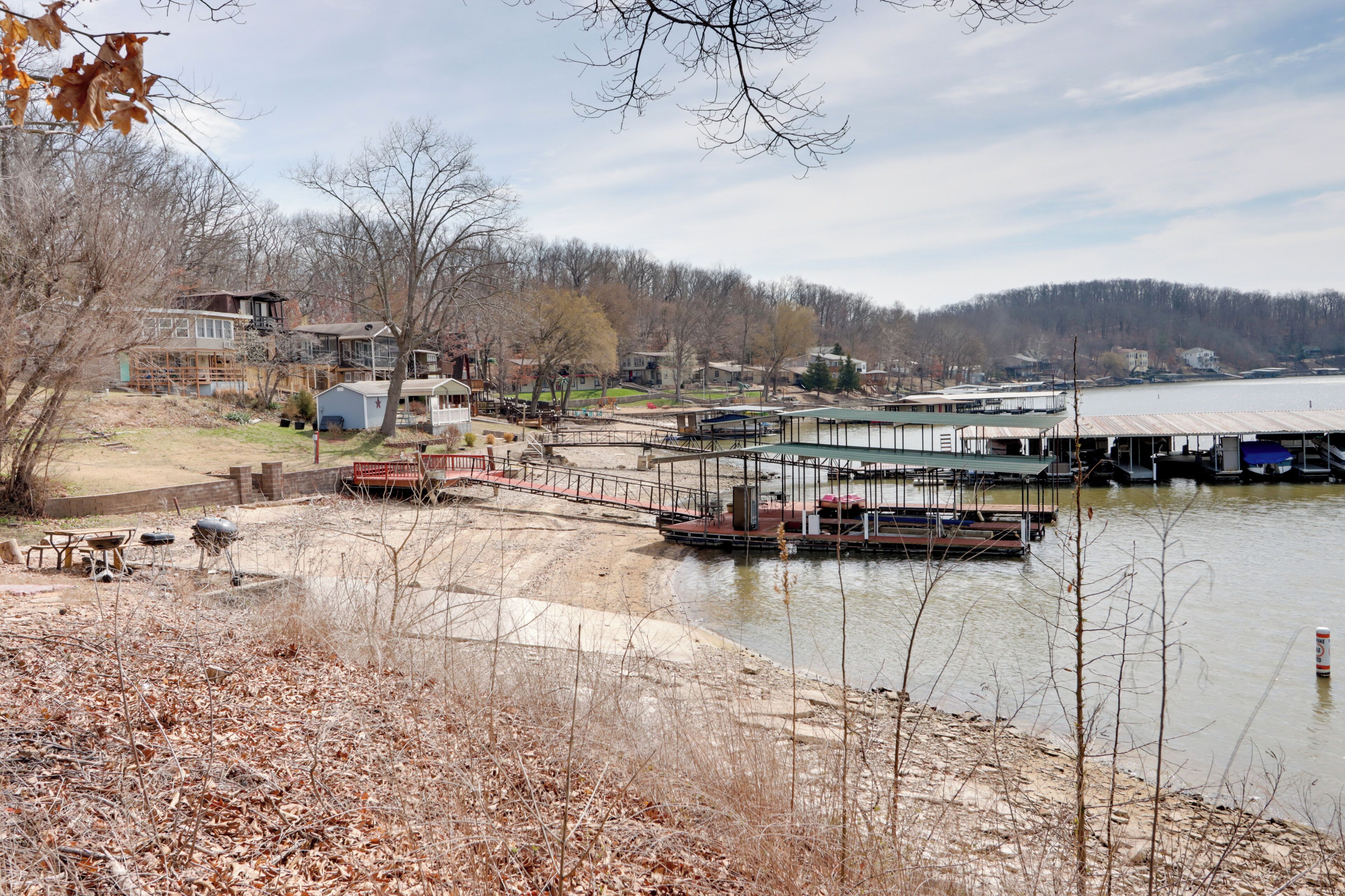 Vista al río con un muelle, un área de picnic y casas al fondo.