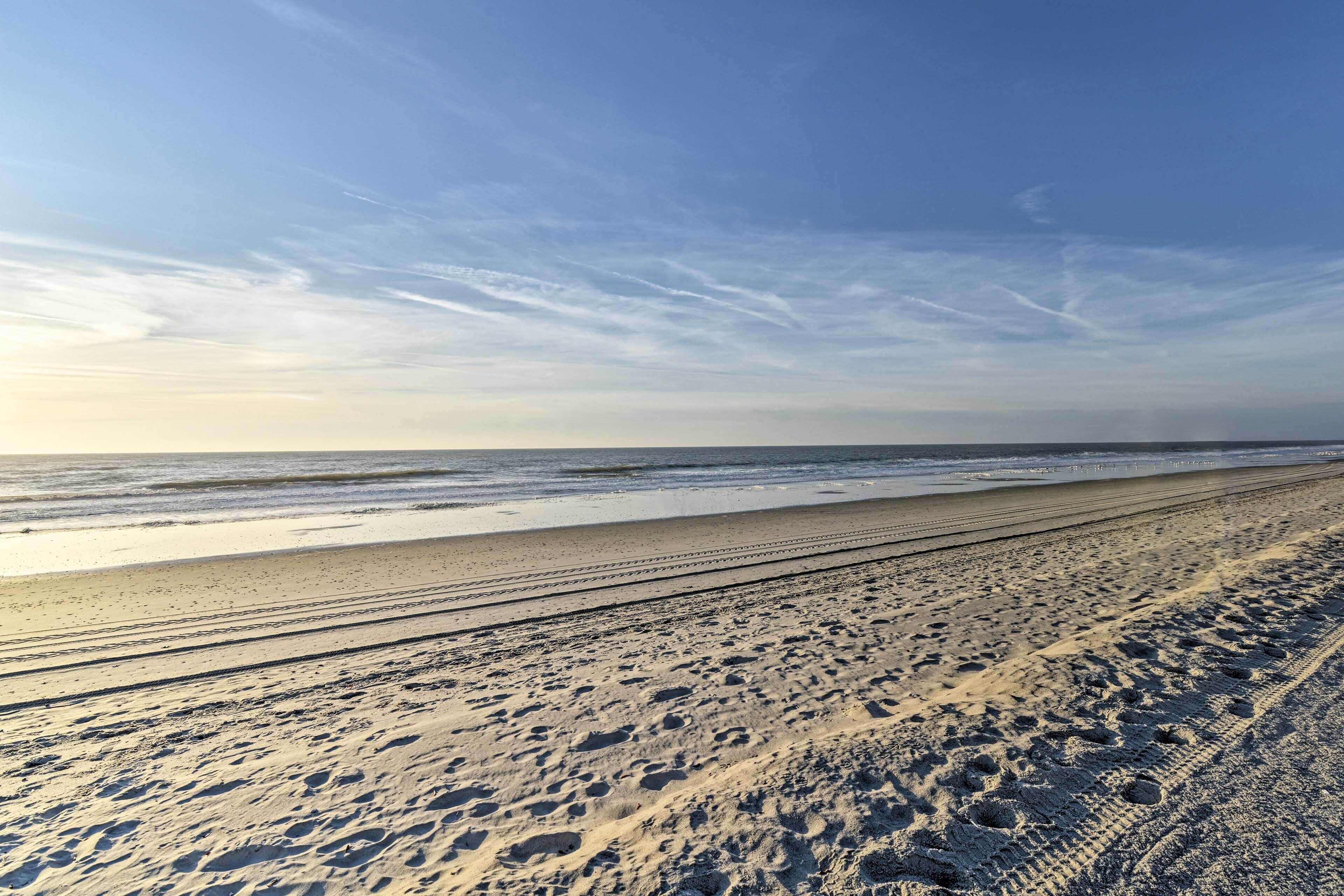 A wide sandy beach with visible tire tracks and footprints.