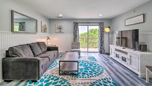A living room with a grey sofa, a coffee table, a white cabinet, and a large window with curtains.