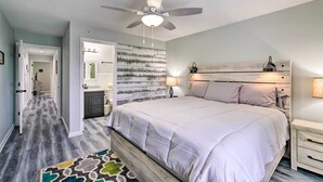 A bedroom with a large bed, a ceiling fan, a nightstand, and a wall-mounted lamp.