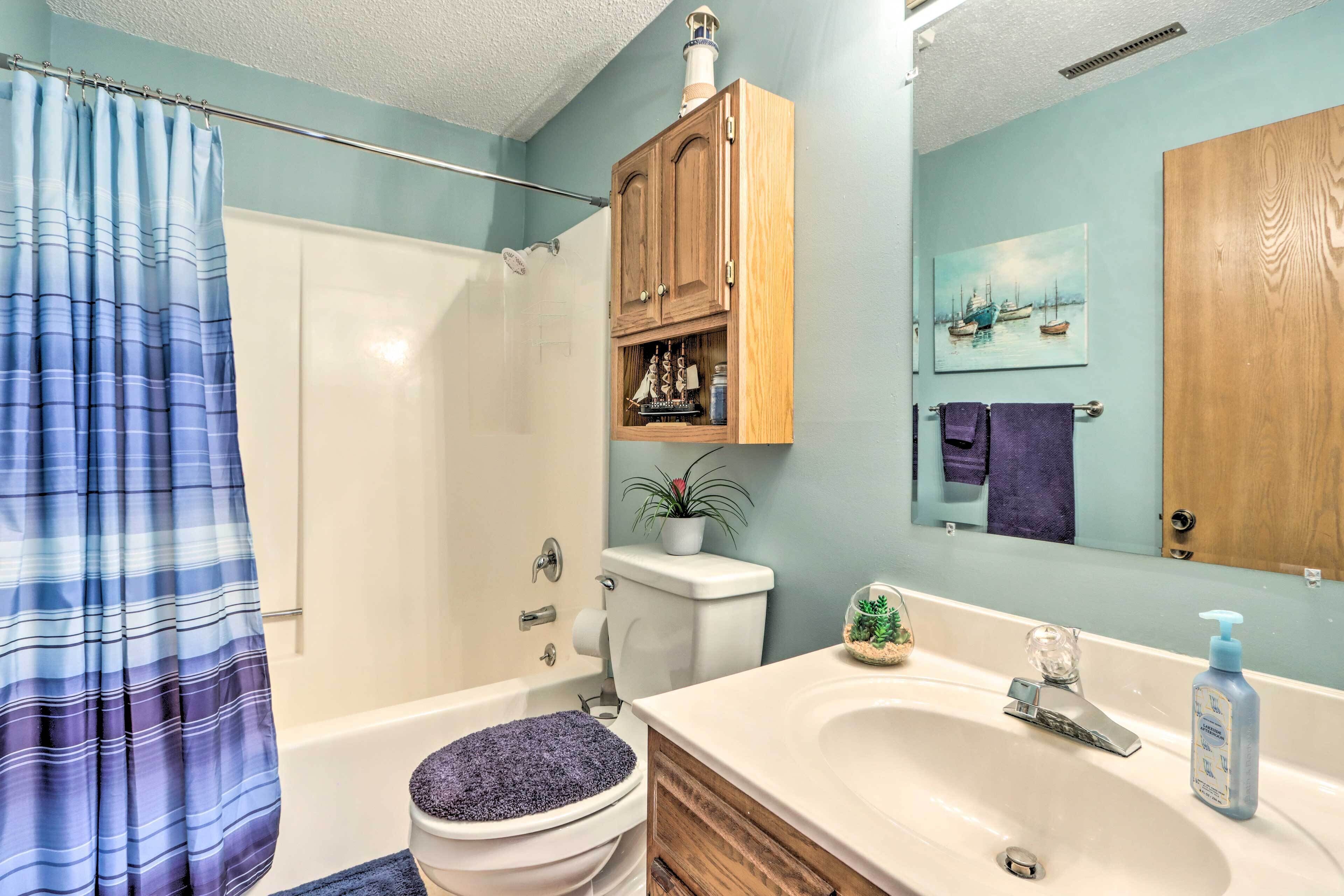 Un baño con bañera, inodoro, armario de madera, lavamanos y cortina de ducha.