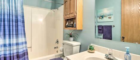 Un baño con bañera, inodoro, armario de madera, lavamanos y cortina de ducha.
