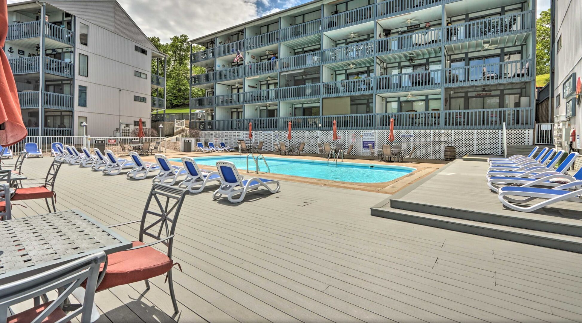 A poolside area with lounge chairs and a swimming pool, surrounded by a building with multiple balconies.