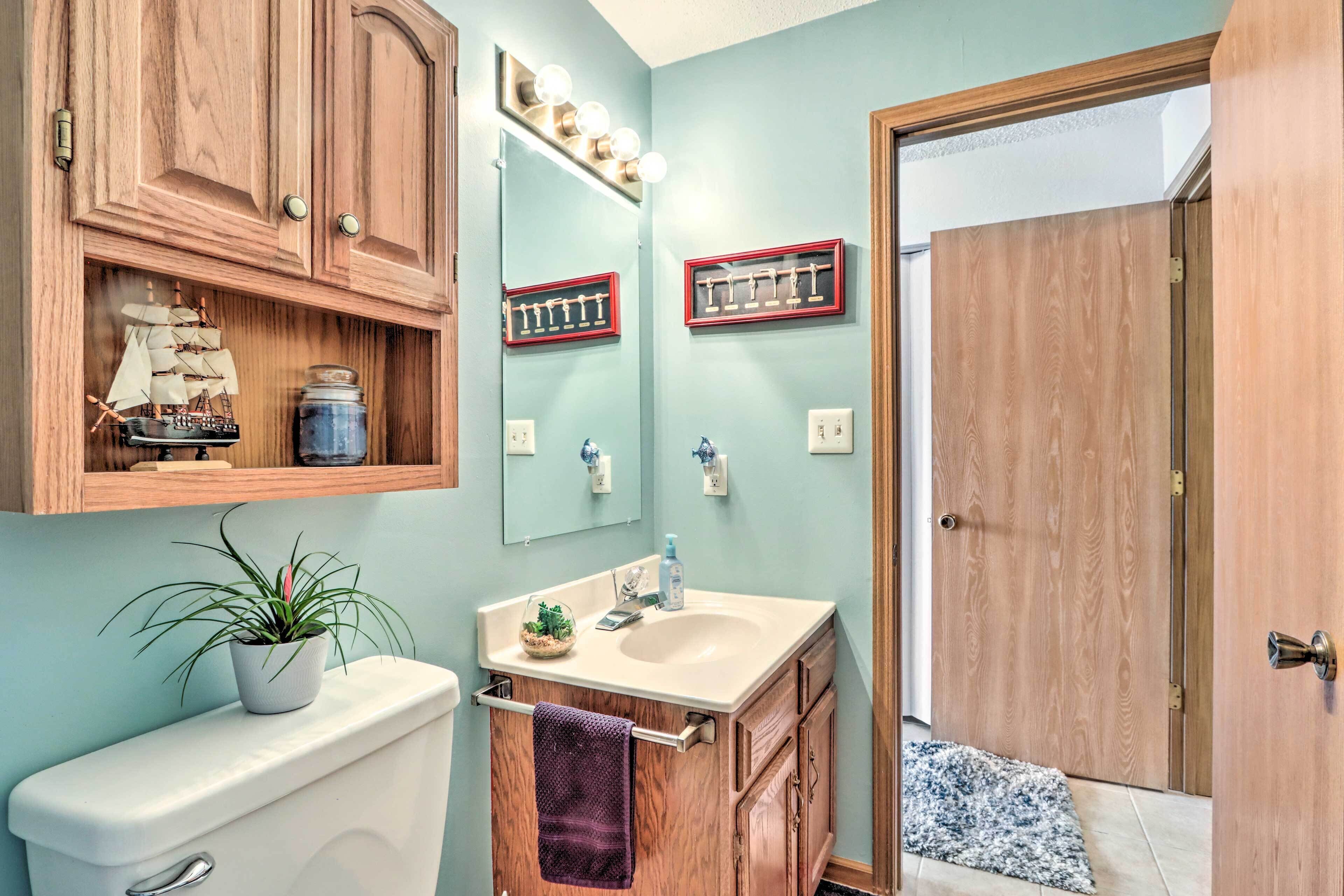 A bathroom with wooden cabinets, a toilet, a sink with a mirror, and a ship model on the cabinet.