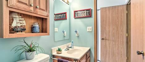 A bathroom with wooden cabinets, a toilet, a sink with a mirror, and a ship model on the cabinet.