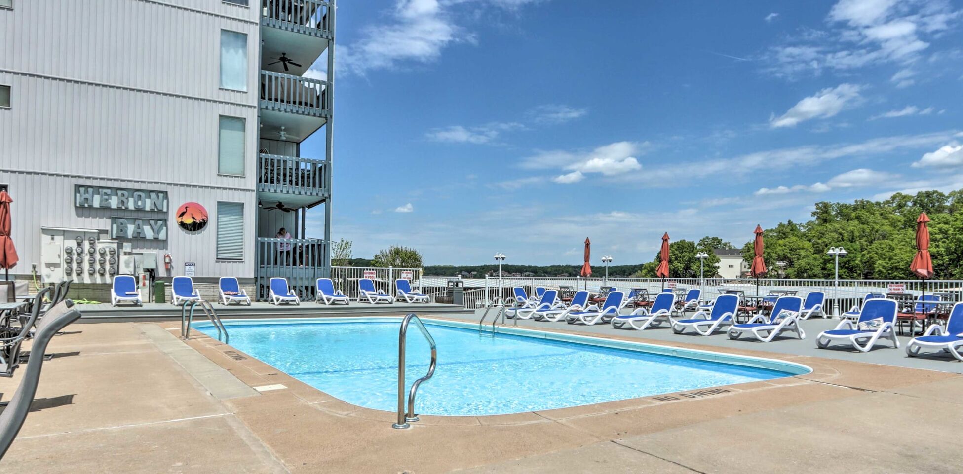Ein Swimmingpool mit blauen Liegestühlen und ein Gebäude im Hintergrund, auf dem 'HERONI BAY' steht.