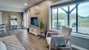 A spacious living room with a large window, a television, a plant, and a cozy seating area. - Waterfront Home Near Mark Twain National Forest (Poplar Bluff)